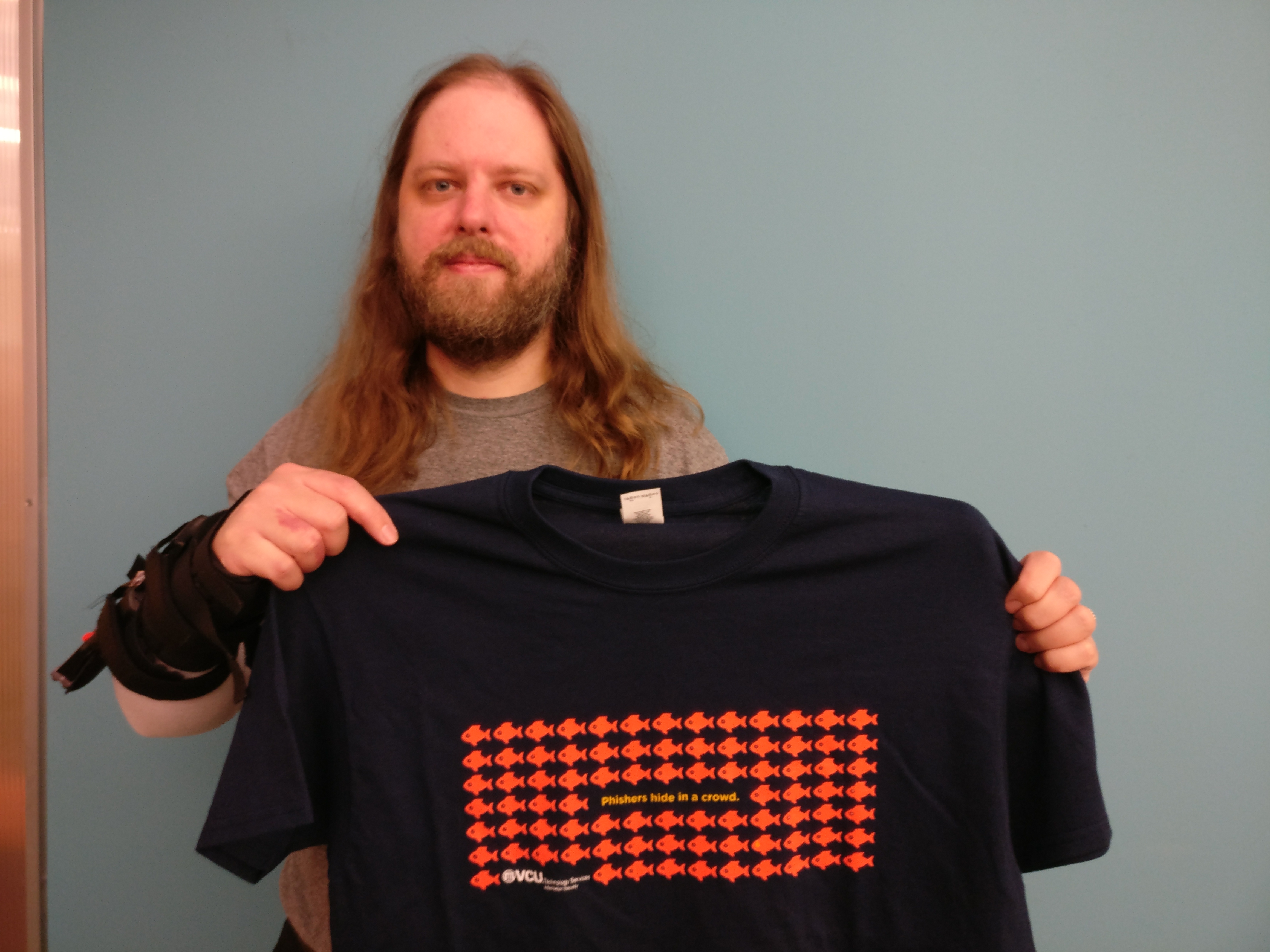 Photo of Matthew Martin holding a phishers hide in a crowd tee.